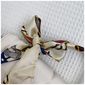 Detail of white quilted handbag featuring a vintage floral silk scarf tied to the handle