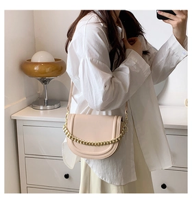 Detail of cream saddle bag featuring a bold gold chain and adjustable leather strap