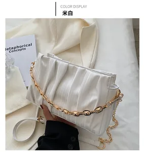 Macro detail of creamy white pleated shoulder bag with gold chain and strap on white fabric