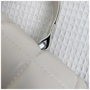 Detail of white quilted crossbody bag showing silver square metal buckle and stitching