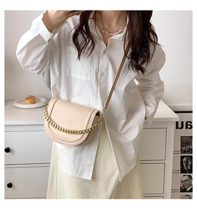 Detail of a beige leather saddle bag with gold chain strap and adjustable shoulder strap