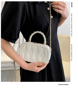 Detailed view of white quilted clutch bag with woven handle and gold chain strap