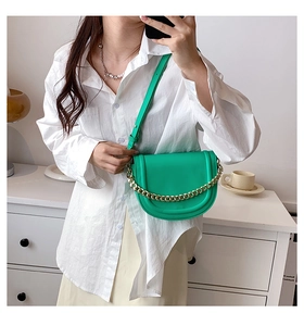 Detail of bright green saddle bag with gold chain and thin shoulder strap on white shirt