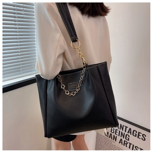 Detail of black leather tote bag with gold floral chain and white contrast stitching