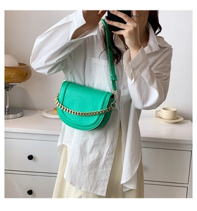 Detail of bright green saddle bag with gold metal chain and adjustable leather strap