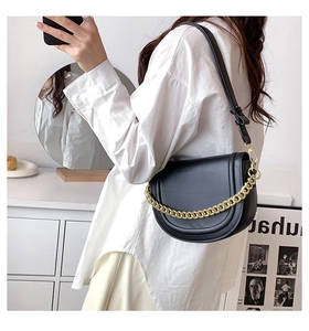 Detail of black saddle bag with gold chain strap worn by model in a minimalist home setting