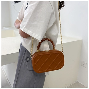 Detail of a brown quilted crossbody bag with a gold chain strap and twisted handle