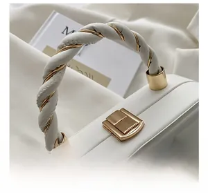 Detail of white leather bag featuring a twisted woven handle and gold hardware lock