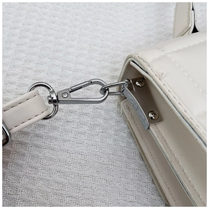 Detail of silver carabiner clip and quilted leather texture on a white fashion bag