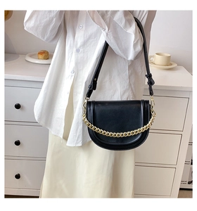 Detail of a black saddle bag with thick gold chain decoration and adjustable strap