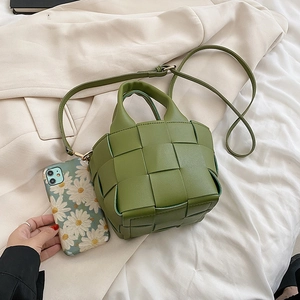 Green mini woven bucket bag with top handle and strap shown next to a smartphone