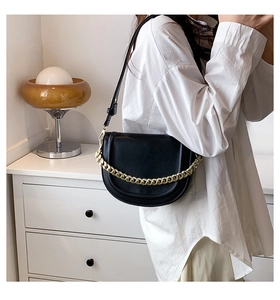 Detail of a chic black saddle bag with a chunky gold chain and leather strap