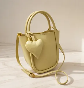 Dettaglio di una borsa a secchiello giallo crema con doppi manici e ciondolo a cuore