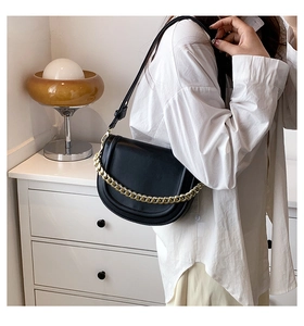 Detail view of black saddle bag featuring thick gold chain strap on white shirt