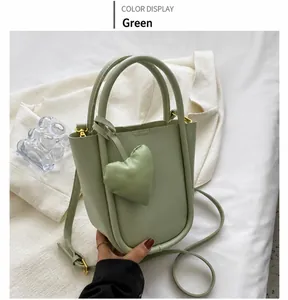 Dettaglio della borsa a secchiello in pelle verde chiaro con ciondolo a cuore su tessuto