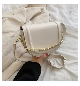 Close-up of a cream saddle bag featuring a chunky gold chain and thin leather strap