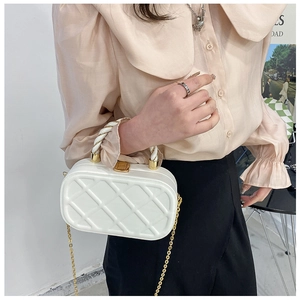 Detail of white quilted crossbody bag featuring a golden chain strap and textured handle