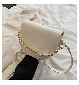 Close-up of cream saddle bag featuring matte faux leather and gold chain detail