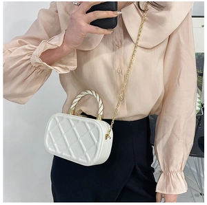 Detail of white quilted crossbody bag with golden chain and twisted handle on person