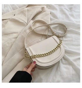 Chic beige saddle bag with gold chain and strap on minimalist fabric background