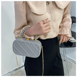 Detailed view of grey quilted crossbody bag with gold chain and twisted handle worn by model