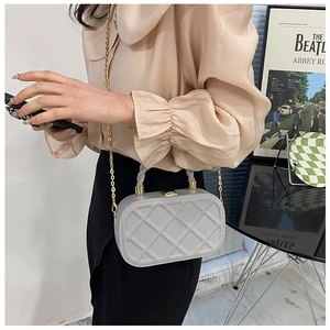 Detail of light gray quilted box bag with a twisted handle and gold chain strap