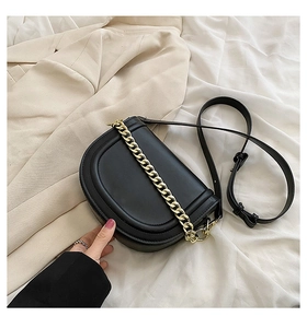 Close-up of black half-moon saddle bag with thick gold chain decoration on fabric