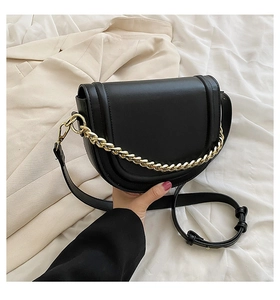 Detail of black saddle bag with gold chain strap held against a beige blazer