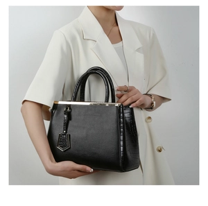Detail of black leather handbag with crocodile texture and gold hardware on white blazer