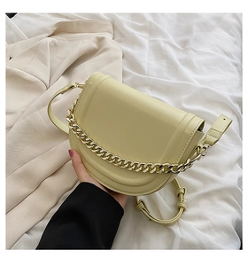 Fashionable cream yellow saddle bag with chunky gold chain detail on soft white fabric