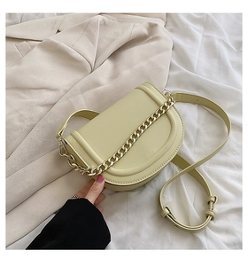 Flat lay of a yellow saddle bag with gold chain strap on a beige blazer and white cloth
