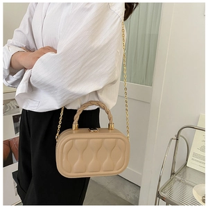 Detail of beige quilted box bag featuring golden chain strap and textured handle