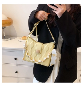 Detail of yellow quilted chain bag with heart scarf and wooden buckle held by model