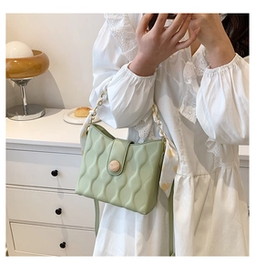 Detail of light green quilted crossbody bag featuring wooden button and silk scarf chain