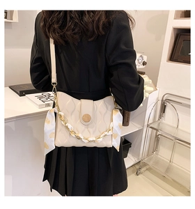 Detail of cream white quilted crossbody bag with gold chain and silk scarf on a shoulder