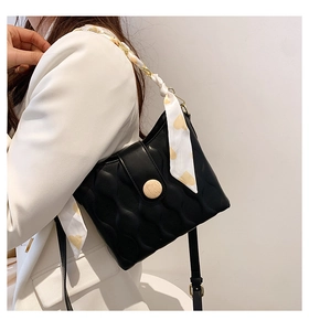 Detail of black quilted crossbody bag with silk scarf chain strap on white blazer