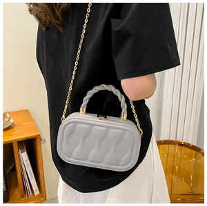 Detail of light gray box bag featuring wave texture and twisted top handle with gold chain