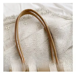 Detail shot of the beige pleated texture and brown faux leather handle of the handbag