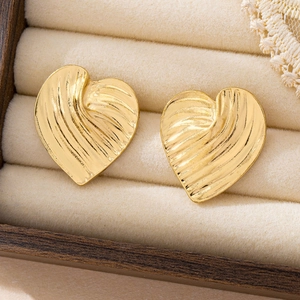 Macro shot of gold-plated heart studs with radial wave texture on beige velvet