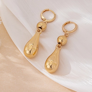 Close-up of golden teardrop pendant earrings on white silk fabric background