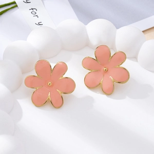 Gros plan sur les boucles d'oreilles fleurs en émail rose doux avec coeur doré