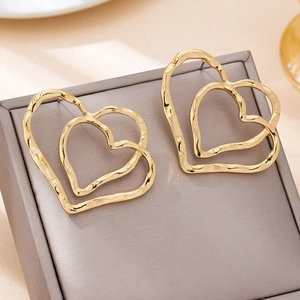 Double layered heart stud earrings with hammered gold texture on grey jewelry display box