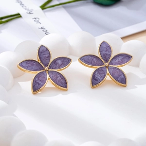 Detailed view of purple enamel flower earrings on a textured plate with decorative ribbon