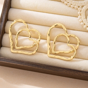 Detail view of gold double heart stud earrings with vintage texture on beige velvet