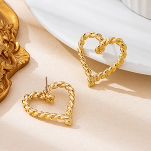 Gedrehte goldene hohle Herzohrstecker mit Vintage-Spiralseil-Textur auf beiger Oberfläche