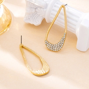 Elegant gold teardrop earrings with crystal accents on a minimalist artistic background