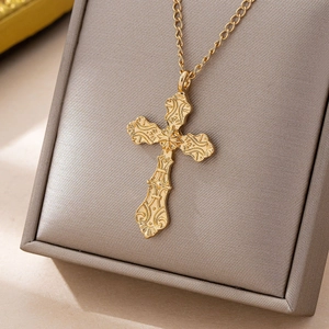 Golden Gothic cross necklace with baroque engraved relief on a gray jewelry stand