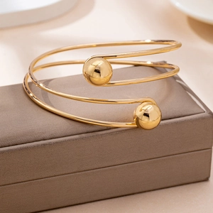 Elegant gold spiral open cuff bracelet with polished metal spheres on a jewelry box