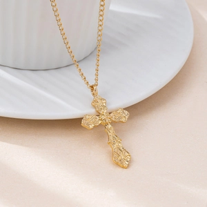Golden Gothic cross necklace with baroque engravings on white ceramic cup background