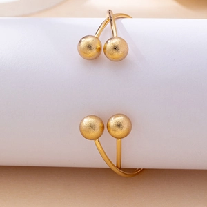 Minimalist gold-finished open bangle with matte texture and spherical ends on white pedestal
